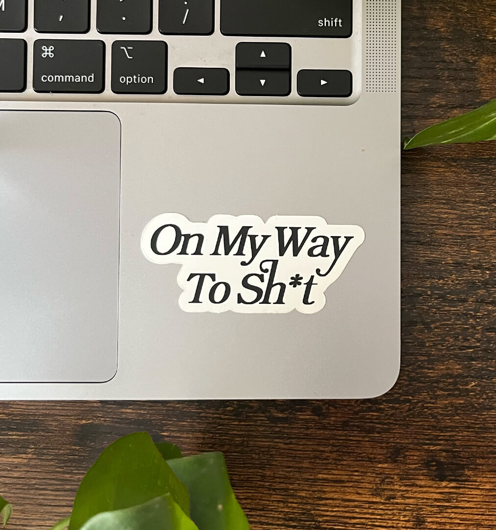 White sticker with the text "On My Way To Sh*t" written in elegant text, on the corner of a laptop.