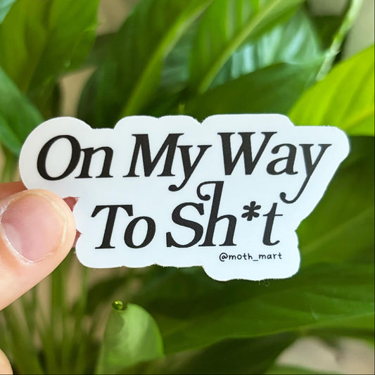 Dye cut sticker with the text "On My Way To Sh*t" held in front of green houseplants.