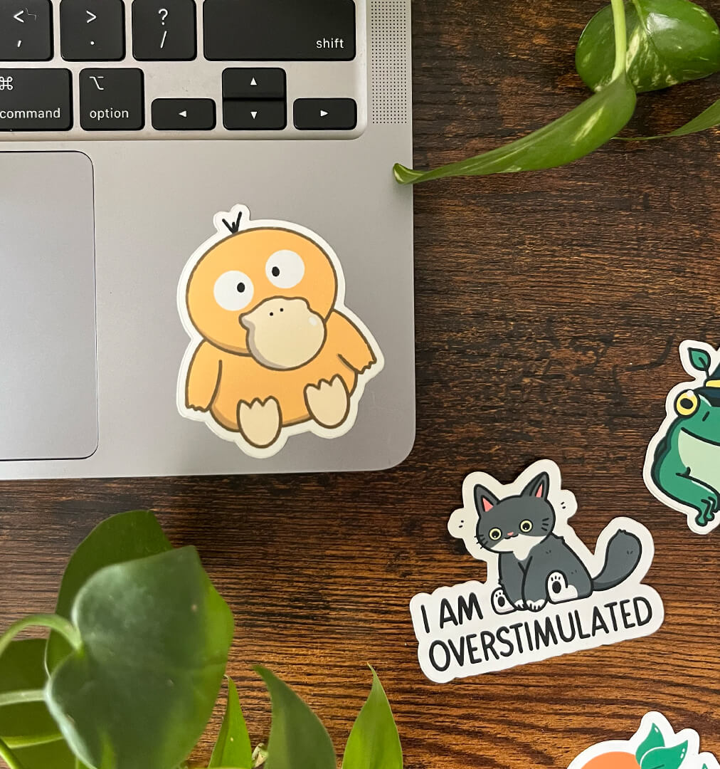 Yellow duck sticker sitting and crosseyed with a headache on the corner of a laptop. Three stickers sit off to the side. 