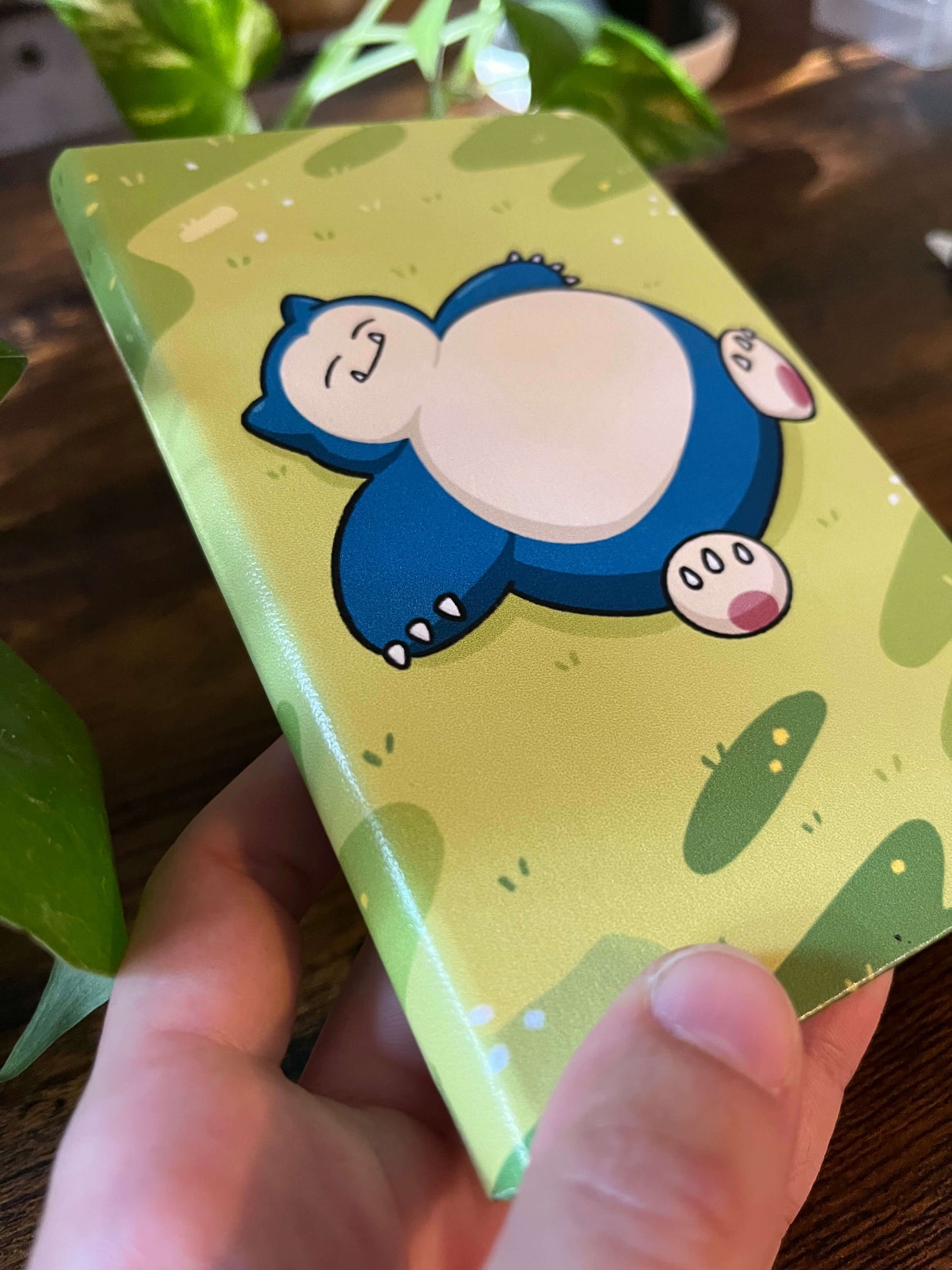 A notebook held by a hand over a wood table. Notebook cover depicts a large blue creature.