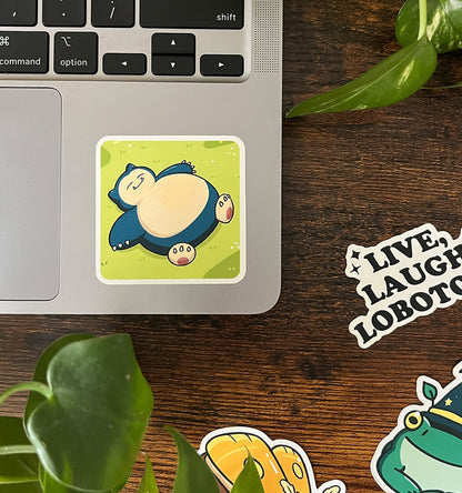 Laptop sticker of blue creature laying in the grass.