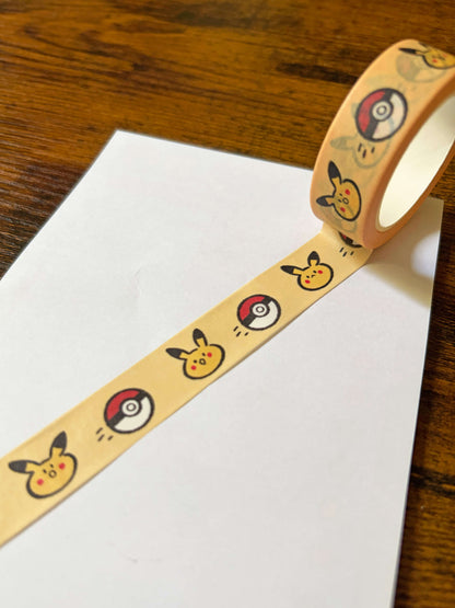 a partially unrolled yellow washi tape with yellow critters and red balls on a white sheet on a wood background.